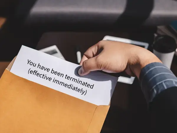 a photo of a person pulling a piece of paper that says "you have been terminated (effective immediately) out of a manila envelope